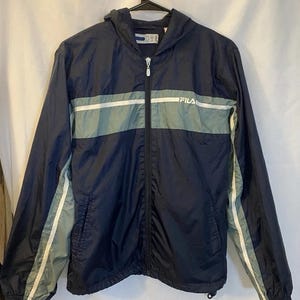 May include: Navy blue hooded windbreaker jacket with a full zipper closure. The jacket features a horizontal gray stripe across the chest and white stripes down the sleeves. The brand name "FILA" is visible on the chest.