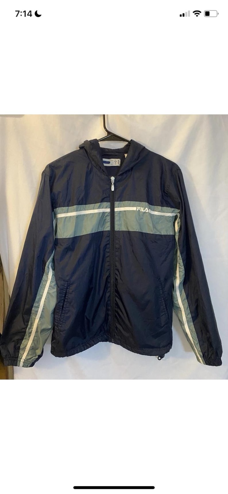May include: Navy blue hooded windbreaker jacket with a full zipper closure. The jacket features a horizontal gray stripe across the chest and white stripes down the sleeves. The brand name "FILA" is visible on the chest.