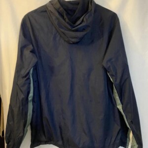 May include: Navy blue hooded jacket with a drawstring hem and a light green stripe detail on the sleeves. The jacket is hanging on a black hanger against a white background.