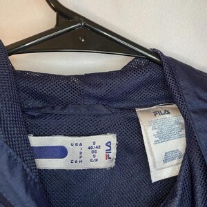 May include: Navy blue Fila jacket with a mesh lining. The tag indicates a size S for the USA, with measurements of 40/42. The jacket is hanging on a black hanger.