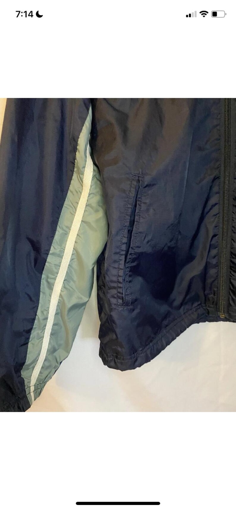 May include: Navy blue windbreaker jacket with a light blue and white stripe detail on the sleeve. The jacket has a zipper closure and a pocket. The material appears to be a lightweight nylon or similar fabric.