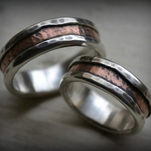 Op de afbeelding: Twee zilveren trouwringen met een gehammerde afwerking en een koperen inlay.