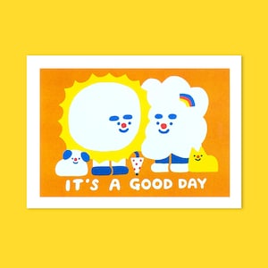 Peut inclure: Impression d'art orange avec un soleil souriant et un nuage avec un arc-en-ciel, accompagnés d'un chien et d'une créature jaune. Le texte "IT'S A GOOD DAY" est imprimé en blanc. L'œuvre a un style joyeux et cartoon.