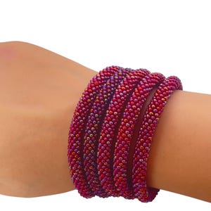 May include: A beaded bracelet in shades of red and purple is wrapped around a wrist. The bracelet is made of small, round beads, creating a textured surface. The bracelet is a vibrant accessory.