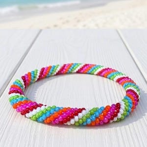 May include: A circular bracelet constructed from small, multi-colored glass beads arranged in a repeating diagonal spiral pattern. The beads feature a vibrant palette of red, orange, pink, white, green, and blue, creating a continuous textured loop.