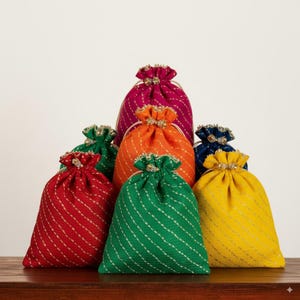 Puede incluir: Una colección de coloridas bolsas con cordón en varios tonos, incluyendo rojo, verde, naranja, amarillo, rosa y azul. Cada bolsa presenta un patrón de rayas diagonales y un cierre decorativo con cuentas. Las bolsas están dispuestas sobre una superficie de madera.