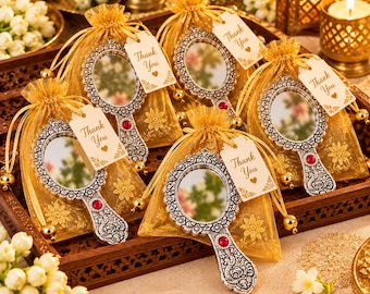 May include: Five silver-toned handheld mirrors with ornate floral detailing and a single red accent stone at the base of the handle. Each mirror is individually packaged in a gold organza drawstring bag with a white tag reading Thank You.