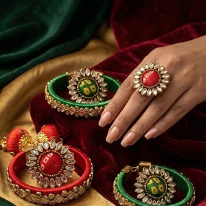 Op de afbeelding: Een verzameling sierlijke sieraden met rode en groene armbanden en een ring. De armbanden zijn gewikkeld in zijde en versierd met goudkleurig metaal en edelstenen. De ring heeft een grote rode middensteen en een bloemmotief.