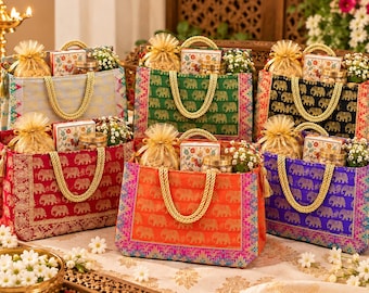 May include: Six rectangular fabric gift bags in light blue, green, black, red, orange, and purple, each featuring a repeating gold elephant pattern, gold braided handles, and filled with small gift boxes, jars, and organza pouches.