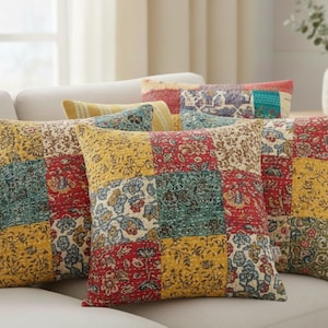 May include: A collection of decorative throw pillows with a patchwork design. The pillows feature a mix of floral patterns in red, yellow, blue, and green. They are arranged on a light-colored sofa, creating a cozy and inviting atmosphere.