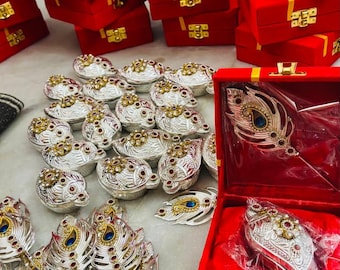 May include: An assortment of ornate silver and gold-toned jewelry pieces, including peacock feather designs and small, round containers. Many items are displayed in red velvet boxes with gold clasps, suggesting a theme of luxury and gifting.