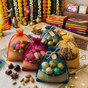 Könnte beinhalten: Eine Auswahl an bunten Geschenktüten, gefüllt mit Pralinen und Muscheln. Die Tüten sind in den Farbtönen Orange, Pink, Türkis und Gelb gehalten und mit dekorativen Verzierungen versehen. Verschiedene Pralinen und Nüsse sind um die Tüten herum verstreut.