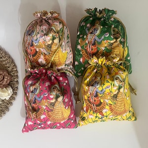 May include: Four drawstring bags in pink, yellow, green, and cream. Each bag features a detailed illustration of figures in traditional attire. The bags have gold-colored drawstrings and are likely used for gifting or storage.