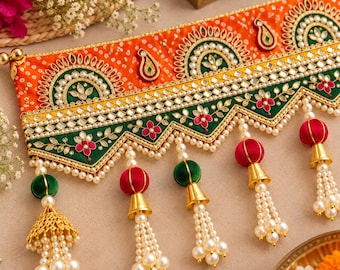 May include: A decorative fabric valance featuring an orange band with white dot patterns and a green scalloped border. It is embellished with gold embroidery, small mirrors, and dangling tassels made of red or green spheres and white pearls.