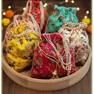 Puede incluir: Una colección de coloridas bolsas con cordón bordadas en una bandeja de madera. Las bolsas son de color rojo, amarillo, rosa, turquesa y crema, adornadas con patrones florales y cordones de cuentas perladas. Una borla dorada cuelga de una bolsa.