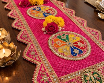 May include: A vibrant fuchsia table runner featuring a textured grid pattern, scalloped edges, and gold metallic embroidery. It is decorated with circular motifs containing colorful floral segments, small mirrors, and artificial pink and yellow flowers.