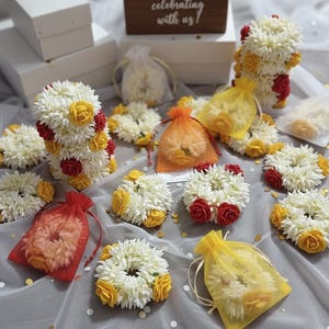 Peut inclure: Diverses guirlandes et compositions florales. Les guirlandes sont blanches avec des accents jaunes et rouges. Certaines sont dans de petits sacs en organza de différentes couleurs. Un panneau en bois indique "celebrating with us!"