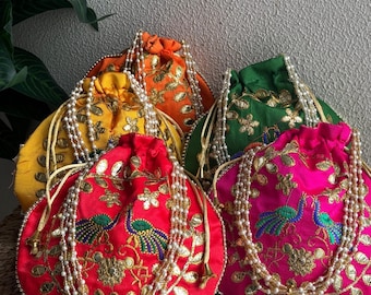 May include: A collection of colorful, embroidered drawstring pouches. The pouches are in shades of red, pink, green, orange, and yellow. Each pouch features gold embroidery and a beaded strap. The pouches are decorated with peacock designs.