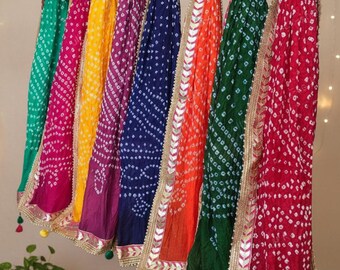 May include: A display of colorful, patterned scarves in shades of green, pink, yellow, purple, blue, orange, and red. Each scarf is adorned with gold trim and small tassels, hanging from a wooden rod. The scarves have a dotted pattern.