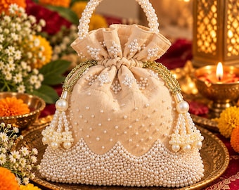 May include: A beige drawstring pouch bag featuring a pearl-beaded handle and a dense border of white pearls along the bottom. The fabric is embellished with scattered pearls and gold-toned braided drawstrings with pearl-adorned tassels.