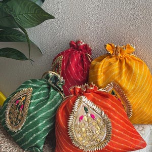 Puede incluir: Una colección de coloridas bolsas con cordón en rojo, verde, naranja y amarillo. Cada bolsa presenta un diseño de cachemira dorado y plateado con detalles florales. Las bolsas están hechas de tela a rayas.