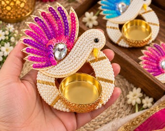 May include: A bird-shaped tea light candle holder crafted with white beads, featuring a fuchsia and purple sequined tail, a clear teardrop-shaped rhinestone accent, and a circular gold-toned metal cup for holding a small candle.