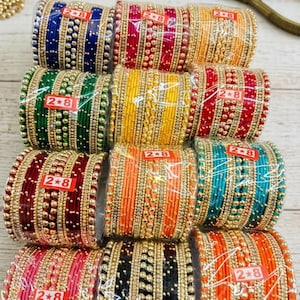 May include: A selection of vibrant bangles in shades of blue, red, green, yellow, orange, and teal. Each set is wrapped and labelled with "2*8". The bangles are decorated with gold-coloured beads and accents.