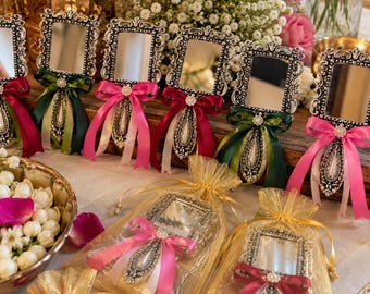 May include: A collection of rectangular handheld mirrors with ornate silver-toned frames, each featuring a decorative handle and a satin ribbon bow in shades of pink, red, or green, with some mirrors packaged in sheer gold drawstring bags.