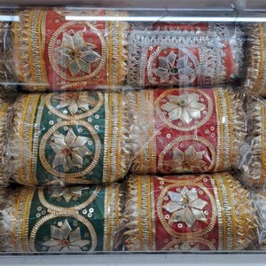 May include: A display of decorative, wrapped, cylindrical items. The items feature a central floral design with silver embellishments, surrounded by gold trim. Colours include red, green, yellow, and gold.