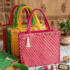 Puede incluir: Una colección de coloridos bolsos de mano con diseños de rayas y adornos decorativos. Los bolsos son de color rojo, verde y amarillo, con asas a juego. Una pequeña borla cuelga de un bolso. Otros artículos incluyen carretes de hilo y un pequeño espejo.