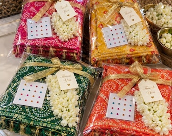 May include: Four folded fabric squares in pink, yellow, green, and orange, each featuring a circular pattern, gold tassels, a white floral cluster, a gold ribbon, a card of colorful adhesive gems, and a tag with the text Thank You.