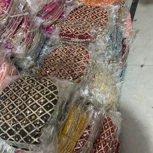Op de afbeelding: Een verzameling kleurrijke, ronde, geborduurde tassen in verschillende kleuren, waaronder roze, oranje, rood en zwart. De tassen zijn versierd met gouden en zilveren versieringen en zijn verpakt in doorzichtig plastic.