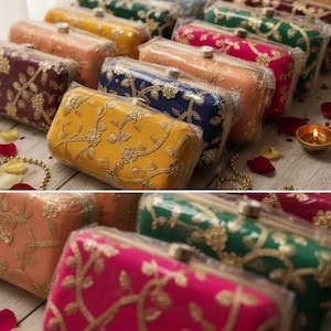 Può includere: Una collezione di pochette rettangolari in vari colori, tra cui giallo, blu, rosa e verde. Ogni pochette è adornata da ricami floreali dorati ed è racchiusa in plastica trasparente. Le pochette sono disposte su una superficie di legno chiaro.