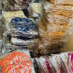 Könnte beinhalten: Eine Sammlung runder, dekorativer Artikel in verschiedenen Farben, darunter Gold, Orange, Blau und Burgunder, sind in durchsichtigem Kunststoff verpackt. Jeder Artikel weist aufwendige Stickereien und Verzierungen auf, was auf ein Handwerks- oder Textilprodukt hindeutet.