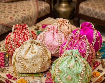 May include: A collection of colorful, embroidered drawstring bags. The bags are in shades of red, pink, green, and cream, adorned with gold accents and pearl-like beads. The bags are likely used for carrying small items.