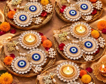 May include: Five gold-toned decorative plates each holding a lit tea light candle, two circular evil eye charms with blue and white beads, and a gold-toned metal charm featuring the Hindi text Shubh Labh, surrounded by small white pearls.