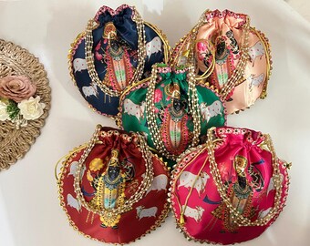 Puede incluir: Cinco coloridas bolsas con cordón y diseños intrincados. Cada bolsa presenta una figura central, vacas blancas y adornos dorados. Las bolsas son en tonos azul marino, rosa, verde, rojo y melocotón, con detalles de perlas y oro.
