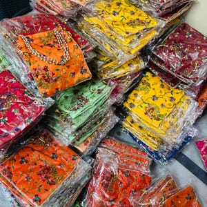 Puede incluir: Una colección de bolsos coloridos con estampados florales en varios tonos, incluyendo naranja, amarillo, rojo y verde. Los bolsos están empaquetados en plástico transparente y parecen estar hechos de un material similar al satén. Algunos bolsos tienen asas con cuentas.