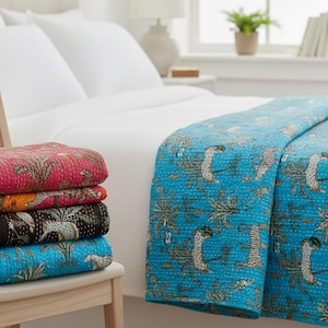 May include: A stack of colorful, patterned quilts in pink, orange, black, and blue, with a matching blue quilt draped over a bed. The quilts feature a repeating design of trees and animals.