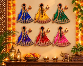 May include: Six wall-mounted decorative cutouts of figures in traditional attire, each holding a lit diya lamp. The figures are arranged in two rows and feature vibrant blue, yellow, green, red, and pink skirts with gold detailing.