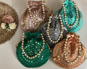 May include: A collection of six satin drawstring pouches in various colors: pink, teal, gray, green, and peach. Each pouch features intricate cut-out designs, embellished with small mirrors and pearl-like beaded straps. The pouches are arranged on a white surface.