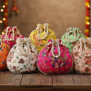 Peut inclure: Une collection de dix pochettes à cordon brodées et colorées, avec des poignées perlées. Les pochettes sont de différentes couleurs, notamment rose, orange, jaune, vert et bleu, et sont décorées de motifs floraux. Elles sont disposées sur une surface en bois.