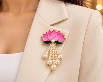May include: A lotus flower brooch featuring pink enamel petals, green enamel leaves, and a central white pearl. Five dangling strands of small white pearls hang from the base, each ending in a larger white pearl, all set in gold-tone metal.