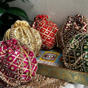 Może przedstawiać: Asortyment ozdobnych woreczków ze sznurkiem w kolorach złotym, czerwonym, bordowym i fuksji. Każdy woreczek jest ozdobiony złotymi akcentami, lustrami i perłowymi koralikami. Woreczki ułożone są na dekoracyjnej tacy.