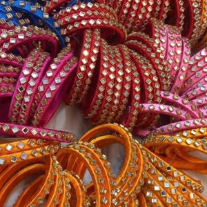 May include: A collection of colorful bangles in shades of blue, red, pink, and orange. Each bangle is adorned with small, square, mirrored embellishments. The bangles are stacked together, showcasing their intricate design and vibrant colors.