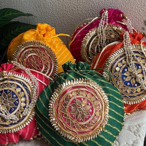 Puede incluir: Una colección de coloridas bolsas con cordón. Cada bolsa presenta intrincados bordados dorados y de colores joya con un diseño floral central. Las bolsas son de color rosa, naranja, amarillo, verde y azul, con detalles de cuentas.