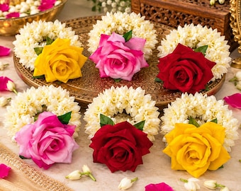 May include: Six circular floral garlands made of white jasmine flowers, each featuring a single large rose in the center. The roses are colored in vibrant shades of yellow, hot pink, and deep red, arranged on a decorative gold-toned tray.