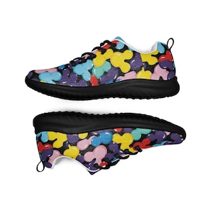Puede incluir: Un par de zapatillas coloridas con suela negra. Los zapatos presentan un patrón de formas abstractas multicolores sobre un fondo oscuro. Los cordones y los ribetes son negros.