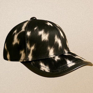 Pode incluir: Boné de beisebol preto e branco com um padrão de pele de vaca. O boné tem uma aba curva e um pequeno botão no topo. Um acessório elegante.