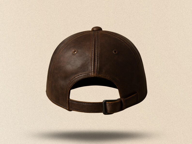 May include: A brown leather baseball cap with a curved brim and adjustable strap. The cap has a button on top and two small ventilation holes. The back of the cap is visible, showing the adjustable strap and buckle.